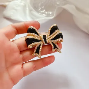 Gros plan d'une broche nœud vintage en émail noir avec perles tenue à la main délicate