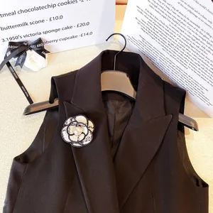 Élégante broche camélia classique en tweed avec perle sur revers de gilet noir.