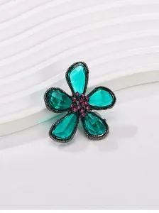 Nahaufnahme einer eleganten Blumenbrosche mit grünen Kristallen und pinker Mitte