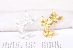 Detail view of gold and silver butterfly brooches with brushed metal texture.