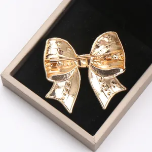Close-up detail of the back pin mechanism on a gold alloy bow brooch in a gift box