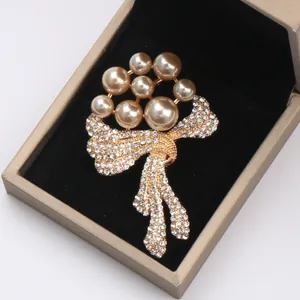 Close-up of a luxury floral pearl brooch with sparkling rhinestones in a gold bow design.