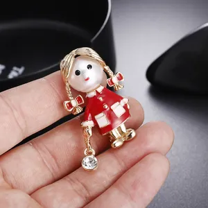 Gros plan d'une broche fille de dessin animé avec tête de perle, émail rouge et strass.