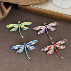 Four colorful enamel dragonfly brooches with rhinestone wings on a textured surface.
