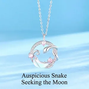 Detail van een zilveren ketting met slang- en maanhanger en roze kristallen