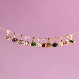 Bunte Edelsteinanhänger an einer Goldkette vor lila Hintergrund, detailgetreue Ansicht.