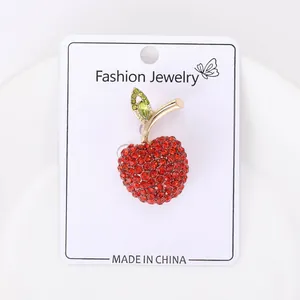 Close-up macro detail of a sparkling red rhinestone apple brooch on white jewelry display card