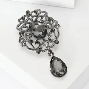 Close-up detail of vintage silver-tone brooch with grey crystals and teardrop pendant.