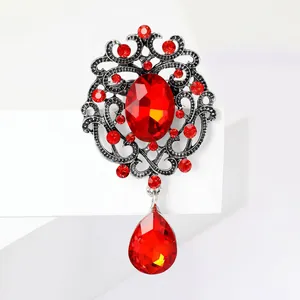 Detailed macro view of a vintage alloy brooch featuring red crystals and a teardrop pendant.