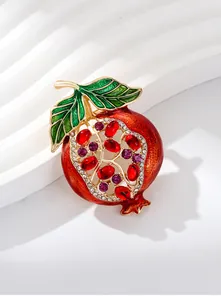 Close-up detail of a vibrant red pomegranate brooch with inlaid rhinestones and green leaves