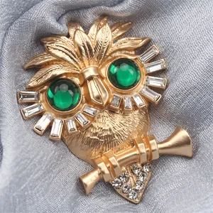 Detailansicht einer goldfarbenen Eulenfibel mit grünen Augen und funkelnden Strasssteinen