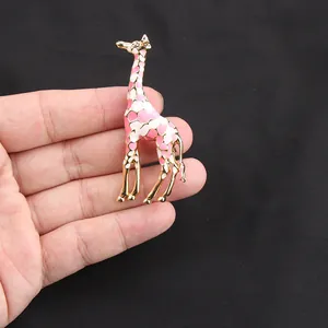 Primo piano di un'elegante spilla a forma di giraffa in smalto rosa e bianco in mano