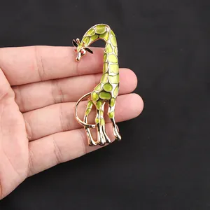 Mano che tiene una spilla a giraffa dettagliata con smalto verde e occhi in cristallo.