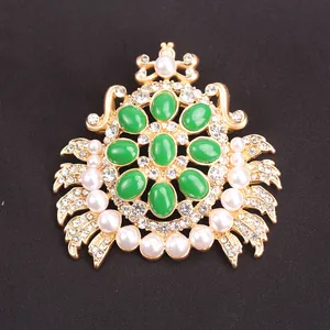 Detailed view of gold crab brooch with green stones, pearls, and crystals