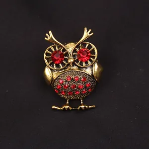Gedetailleerde close-up van een vintage gouden uilenbroche met rode strassteentjes.