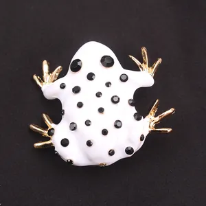 Detail van een witte en gouden kikkerbroche met zwarte strassteentjes op donkere stof