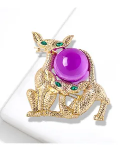 Broche chat vintage dorée avec sphère en verre violet et yeux en pierres vertes.