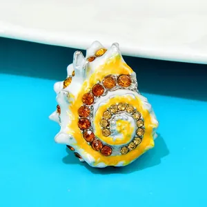 Gedetailleerde weergave van een emaille schelpbrosje versierd met gele strass-steentjes.
