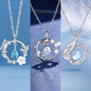 Detailopname van drie zilveren kettingen met vlinder-, dolfijn- en bladhangers in blauw.