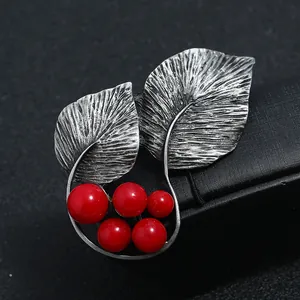 Detailopname van vintage bladbroche met rode bessen en getextureerde zilveren afwerking.