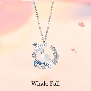 Detailopname van een zilveren walvishanger ketting met witte parel en blauwe accenten