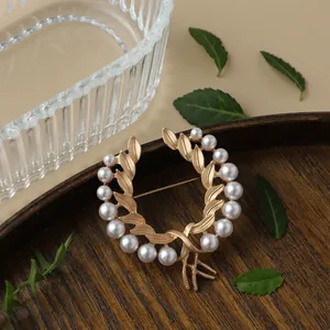 Detailed macro view of a vintage matte gold laurel wreath brooch adorned with white pearls.