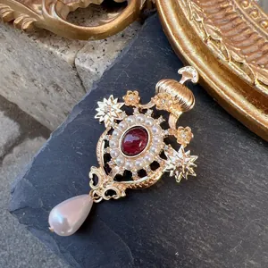 Detailed close-up of a vintage baroque cross brooch featuring pearls and a red crystal center