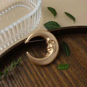 Close-up of vintage matte gold crescent moon brooch with a face design on a wooden tray