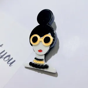 Détail d'une élégante broche en acrylique représentant une fille avec lunettes jaunes