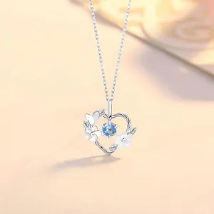 Detail view of a dainty silver floral heart pendant necklace featuring a blue gemstone