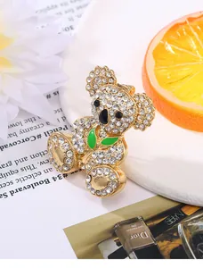 Detail of golden rhinestone koala brooch with green enamel leaves on a decorative tray