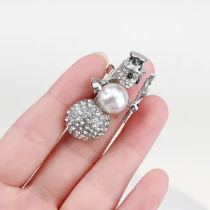 Detail of silver snowman Christmas brooch with rhinestones and pearl held in hand.