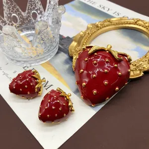 Vista detallada del broche de fresa de esmalte rojo y el juego de pendientes a juego
