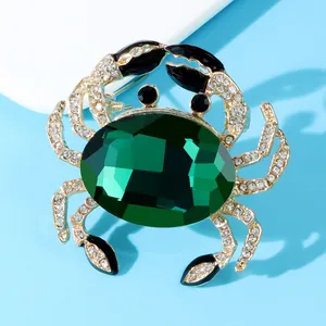 Detailed view of a gold crab brooch with a large emerald green crystal and pavé rhinestones.