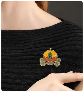 Detail view of a Halloween pumpkin carriage enamel brooch pinned on black knitwear
