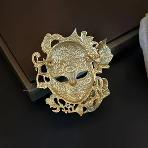 Vue détaillée du dos d'une broche masque vintage dorée avec épingle de sûreté et logo