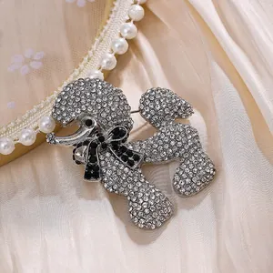 Broche caniche en strass scintillants avec détail de nœud noir sur soie crème.