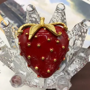 Primer plano detallado de un broche de fresa de esmalte rojo vintage con hojas de oro