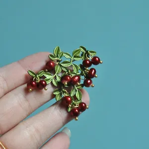 Close-up of vintage cranberry brooch with red pearls and green textured leaves