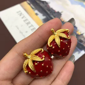 Primer plano detallado de broches de fresa en esmalte rojo estilo vintage con hojas doradas
