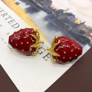 Detalle de primer plano de broche de fresa de esmalte rojo vintage con hojas doradas