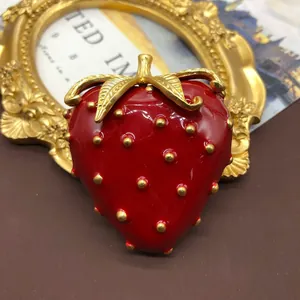 Primer plano de un broche de fresa en esmalte rojo vintage con semillas oro.