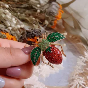 Vista detallada de un broche de abeja vintage con abdomen de fresa y alas de hoja