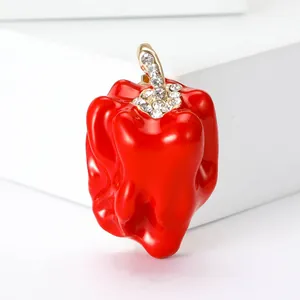 Dettaglio di una spilla a peperone in smalto rosso con strass scintillanti.