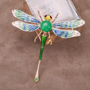 Detailed view of elegant gold dragonfly brooch with green gemstone and enamel wings