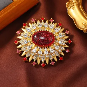 Close-up of a vintage gold sunburst brooch with a red resin center and clear rhinestones.