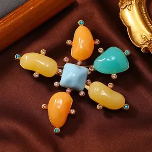 Close-up of vintage enamel cross brooch featuring colorful stones and rhinestones.
