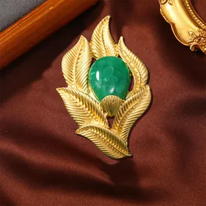 Close-up of a vintage golden leaf brooch featuring a polished green central stone.