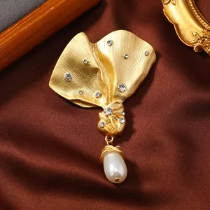 Close-up of vintage gold brooch with sparkling rhinestones and teardrop pearl pendant.