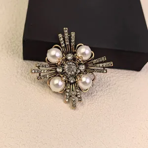 Elegant vintage geometric cross brooch with white pearls and rhinestones on jewelry box